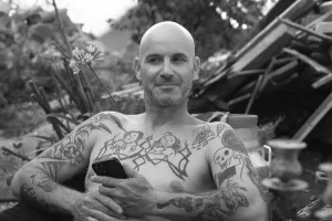 Young man with mobile phone, sitting in the garden with free upper body