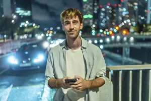 Framed Print : Young man standing outdoors at night smiling at his smartphone