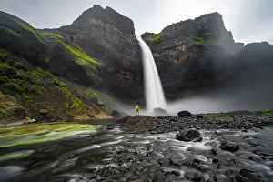 Young man with yellow jacket standing in front of waterfall