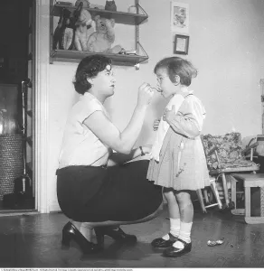 Framed Print : A young mother administers medicine to her daughter with a spoon in her mouth in 1951 Framed Print : A young mother administers medicine to her daughter with a spoon in her mouth in 1951