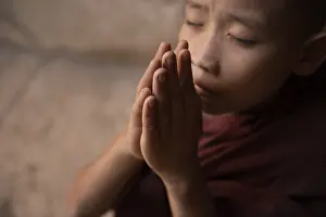Young novice monk praying inside Buddhist temple