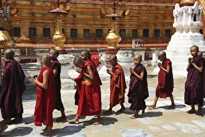 Young novices in red robes in procession in front of a golden pagoda