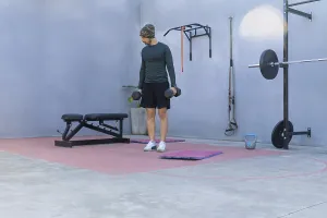 Young sportsman lifting two black dumbbells while engaging in a workout in a private outdoor gym