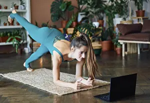 Young sporty woman doing yoga plank watching online exercises on her laptop