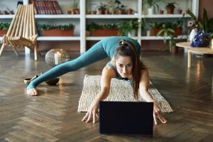 Young sporty woman practicing yoga at home watching online exercises on her laptop