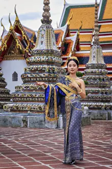 A young Thai woman in traditional clothes stands elegantly before the Grand Palace
