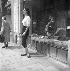 Young woman in 1956. She is standing in front of a shop window on Strandvaegen in Stockholm and maybe she is not aware of the guy in the carpet shop who is sitting inside the window and looking at her admiringly