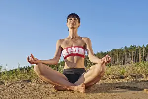 Young woman (30-35) doing yoga on a sunny beach next to a lake