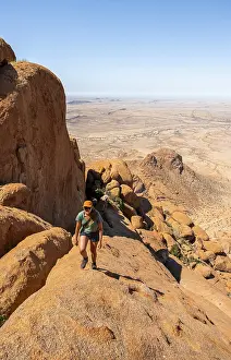 Young woman hiking on rocky hill under blue sky in dry landscape