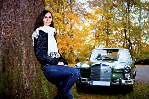 Young woman leaning against a tree in front of a vintage car