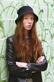 Young woman with long red hair in a stylish black hat and leather jacket in a vibrant green graffiti wall backdrop