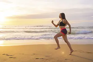 Young woman running along a sandy beach during sunset