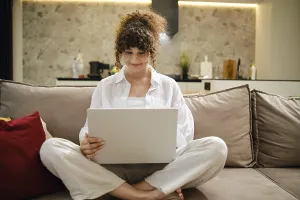 A young woman sits on a couch, laptop on her lap
