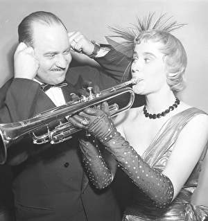 A young woman wearing an evening dress and arm-length gloves plays the trumpet