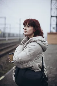 A young woman in a white coat stands at a train station