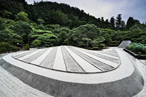 Zen garden of Ginkaku-ji Temple with precise sand patterns and rocks surrounded by green landscape